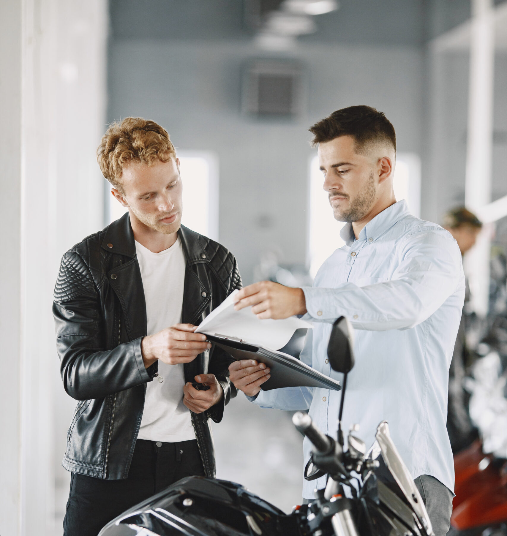 Man choosed motorcycles in moto shop. Guy in a black jacket. Manager with client.